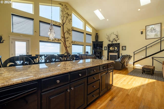 kitchen with high vaulted ceiling, a skylight, light stone countertops, decorative light fixtures, and light hardwood / wood-style floors