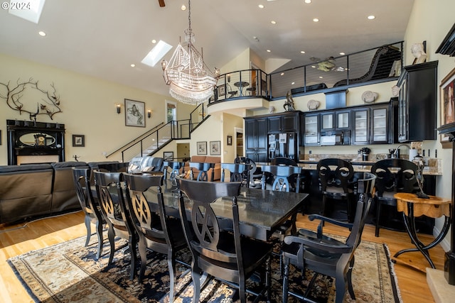 dining space featuring a chandelier, a skylight, high vaulted ceiling, and light hardwood / wood-style flooring