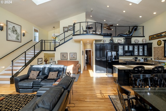 living room with sink, a skylight, high vaulted ceiling, and light hardwood / wood-style flooring