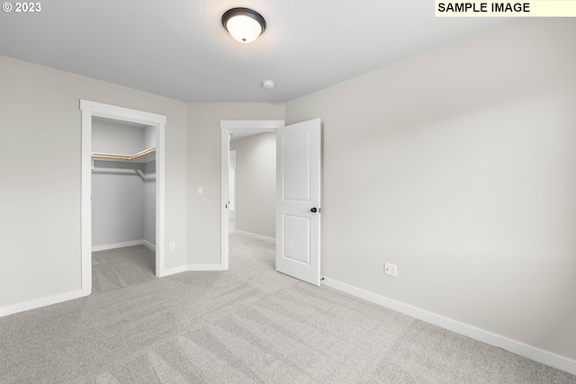 unfurnished bedroom featuring a walk in closet, a closet, and light colored carpet