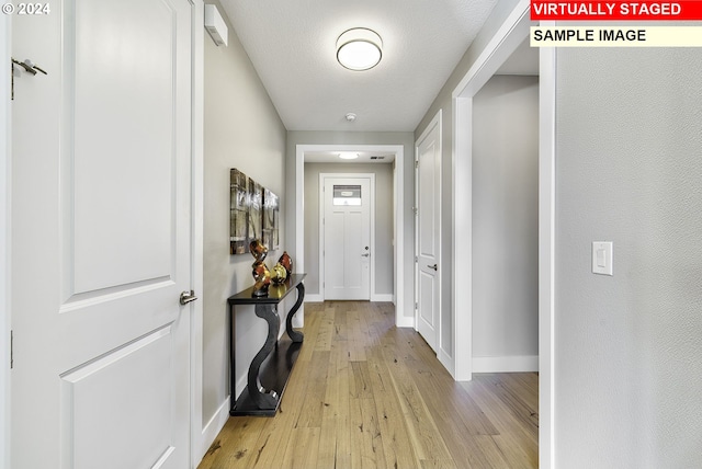 hallway with a textured ceiling and light hardwood / wood-style floors