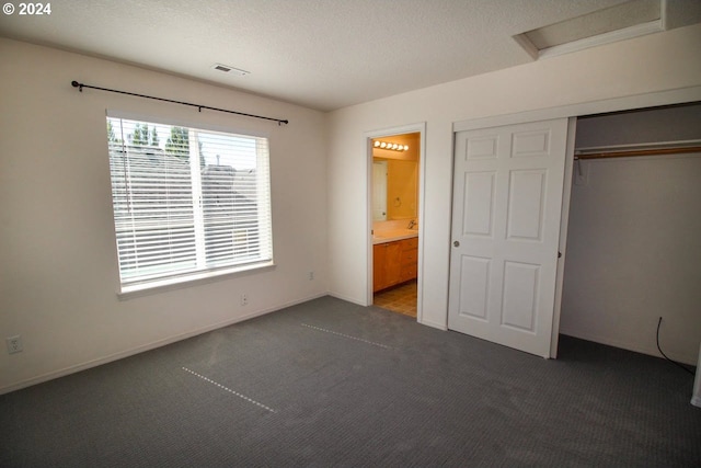 unfurnished bedroom with a textured ceiling, connected bathroom, dark colored carpet, and a closet