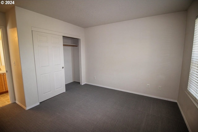 unfurnished bedroom with dark carpet, a closet, and a textured ceiling