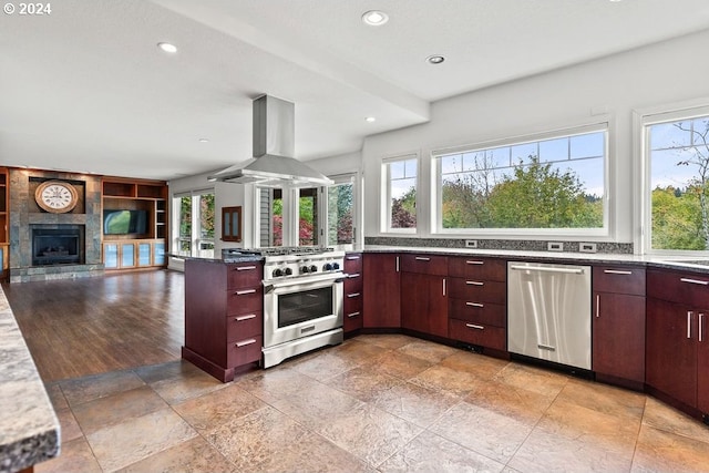 kitchen featuring island range hood, appliances with stainless steel finishes, a tiled fireplace, and a healthy amount of sunlight