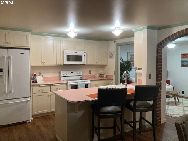 kitchen featuring dark hardwood / wood-style floors, white cabinetry, a kitchen bar, and white appliances