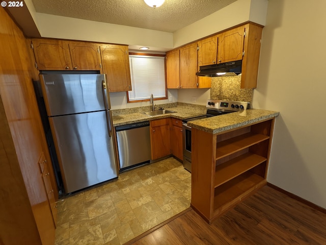 kitchen featuring sink, a textured ceiling, light hardwood / wood-style flooring, stainless steel appliances, and decorative backsplash