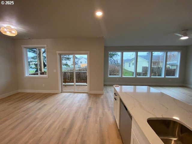 kitchen with light wood finished floors, baseboards, white cabinets, dishwasher, and light stone counters