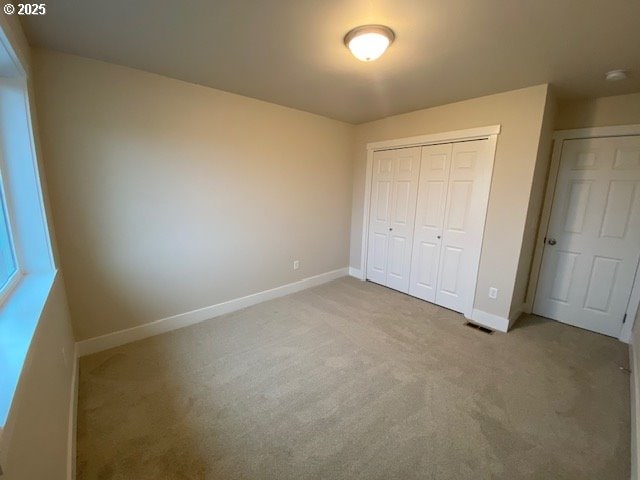 unfurnished bedroom with visible vents, baseboards, a closet, and light colored carpet