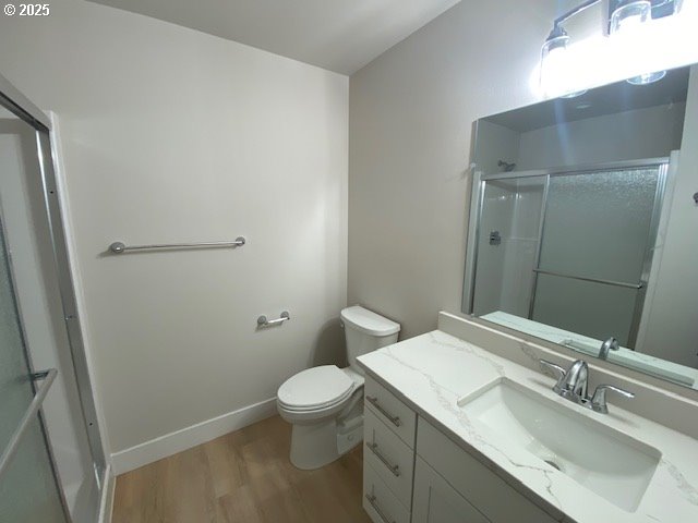 full bath featuring toilet, a shower with shower door, wood finished floors, vanity, and baseboards