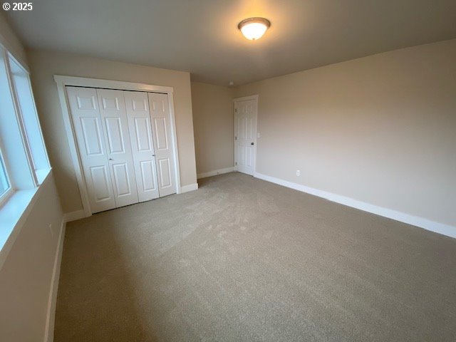 unfurnished bedroom with a closet, light colored carpet, and baseboards