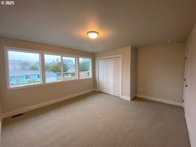 unfurnished bedroom featuring a closet, light colored carpet, visible vents, and baseboards