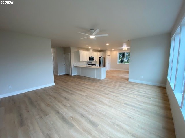 unfurnished living room with light wood finished floors, a ceiling fan, and baseboards