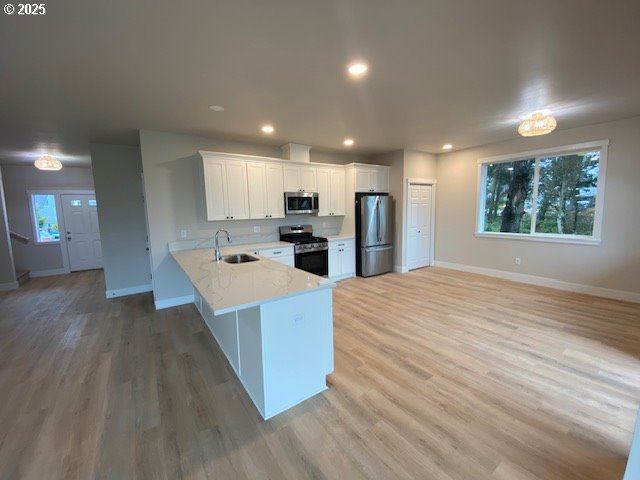 kitchen with white cabinets, light wood-style flooring, appliances with stainless steel finishes, a peninsula, and a sink