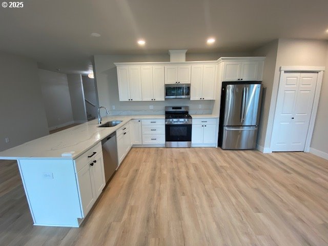 kitchen featuring stainless steel appliances, white cabinets, a sink, light stone countertops, and a peninsula