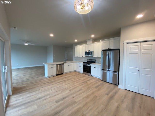 kitchen with open floor plan, a peninsula, stainless steel appliances, light countertops, and white cabinetry