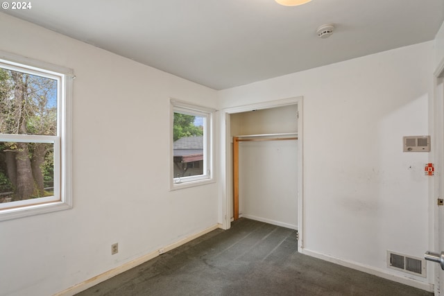 unfurnished bedroom with dark colored carpet, a closet, and multiple windows