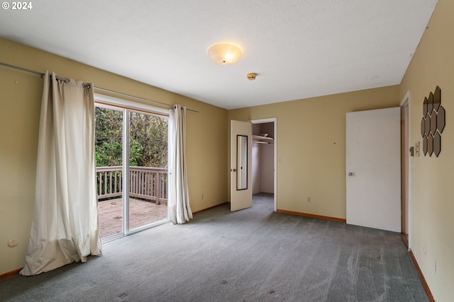 unfurnished bedroom featuring access to outside, a spacious closet, a closet, and dark colored carpet