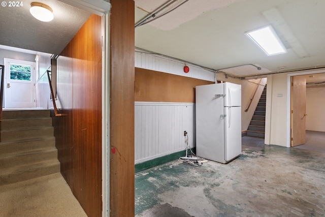 basement featuring white fridge, a textured ceiling, and wooden walls