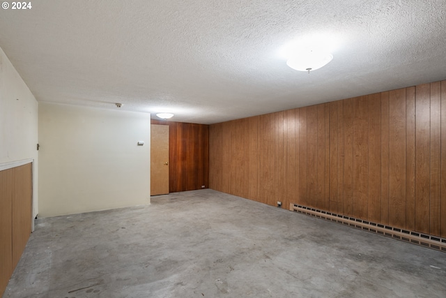 basement featuring baseboard heating, a textured ceiling, and wooden walls