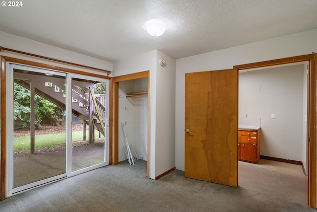 unfurnished bedroom featuring access to exterior, a textured ceiling, light colored carpet, and a closet