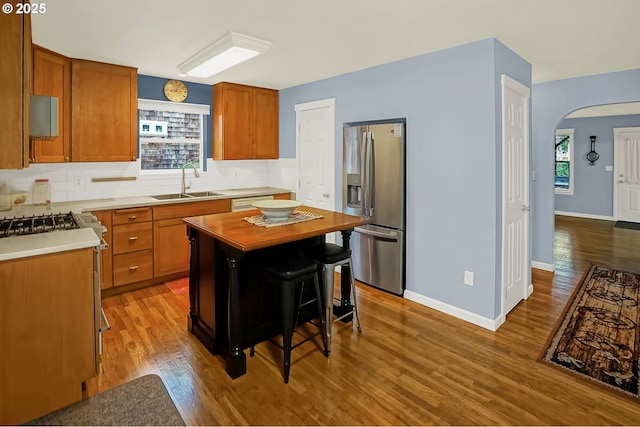 kitchen with sink, a kitchen breakfast bar, stainless steel fridge with ice dispenser, a kitchen island, and hardwood / wood-style flooring