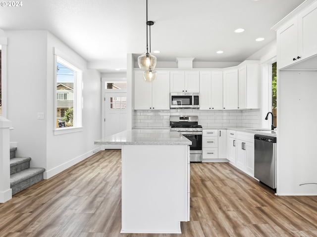 kitchen with stainless steel appliances, white cabinetry, hanging light fixtures, and light hardwood / wood-style flooring