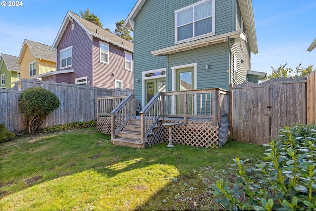 rear view of house with a yard, a wooden deck, and a fenced backyard
