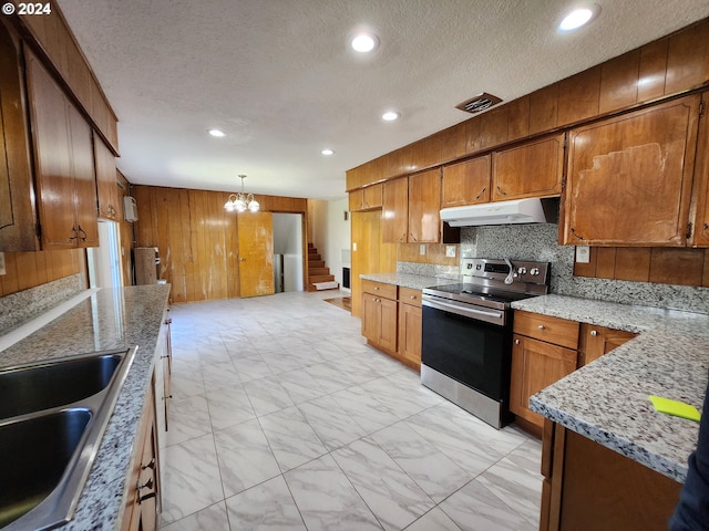 kitchen with wood walls, backsplash, a textured ceiling, pendant lighting, and stainless steel electric range oven