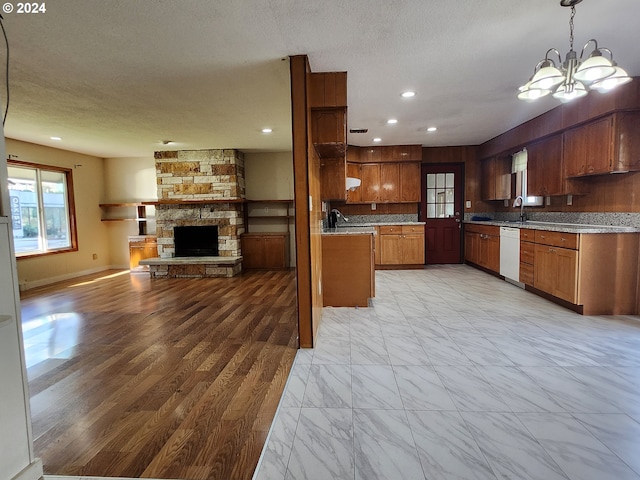 kitchen featuring hanging light fixtures, dishwasher, a stone fireplace, a notable chandelier, and sink