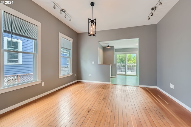 empty room featuring track lighting, light wood-type flooring, and baseboards