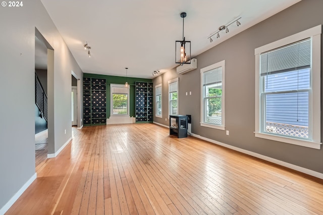 unfurnished living room with a wall unit AC, light wood-style flooring, and baseboards