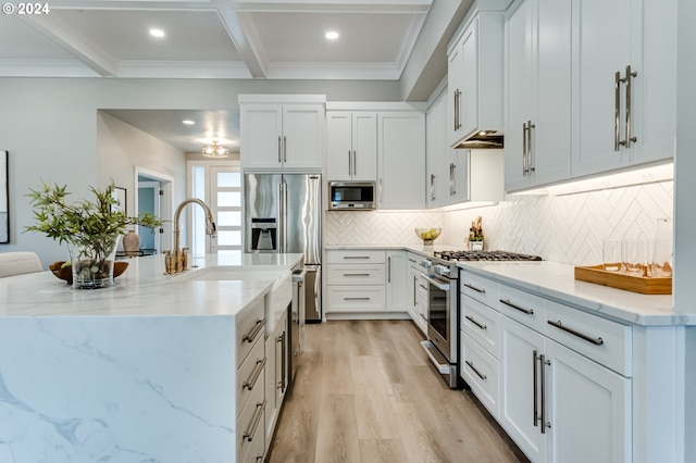 kitchen with appliances with stainless steel finishes, light wood-type flooring, white cabinetry, and beamed ceiling