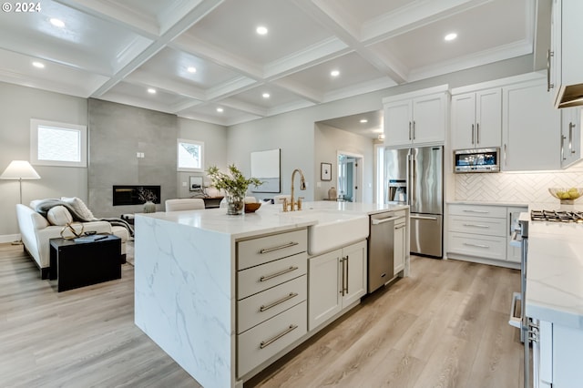 kitchen with an island with sink, light hardwood / wood-style flooring, appliances with stainless steel finishes, a fireplace, and light stone countertops