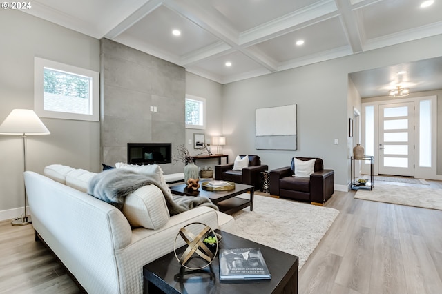 living room with beamed ceiling, coffered ceiling, a tile fireplace, crown molding, and hardwood / wood-style floors