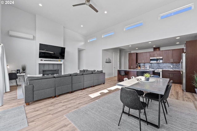 dining space featuring ceiling fan, a tile fireplace, light hardwood / wood-style floors, and a towering ceiling