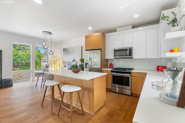 kitchen featuring stainless steel appliances, a kitchen island, light hardwood / wood-style floors, white cabinetry, and hanging light fixtures