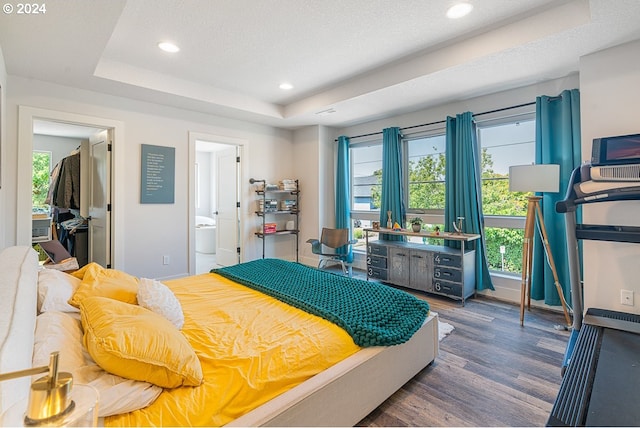 bedroom featuring a textured ceiling, dark hardwood / wood-style flooring, ensuite bathroom, and a tray ceiling