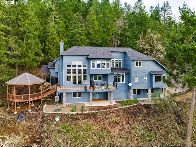 rear view of property featuring a patio, a shingled roof, a chimney, and a wooden deck