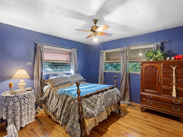 bedroom featuring ceiling fan, light hardwood / wood-style floors, and a textured ceiling