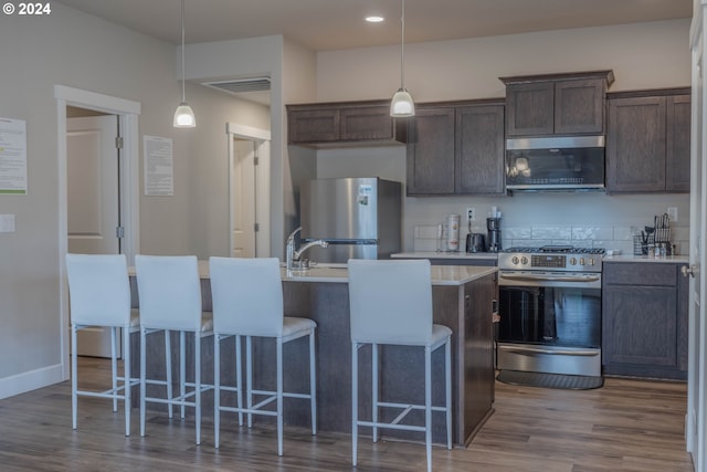 kitchen with dark wood finished floors, stainless steel appliances, light countertops, a kitchen island with sink, and dark brown cabinetry