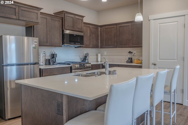 kitchen with light countertops, appliances with stainless steel finishes, a sink, and dark brown cabinetry