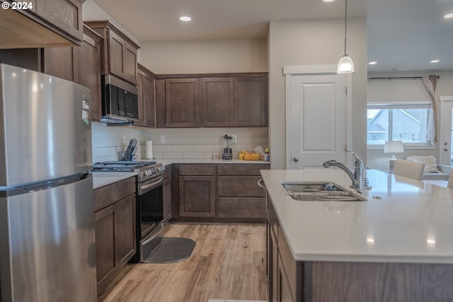 kitchen featuring appliances with stainless steel finishes, hanging light fixtures, light countertops, light wood-type flooring, and a sink