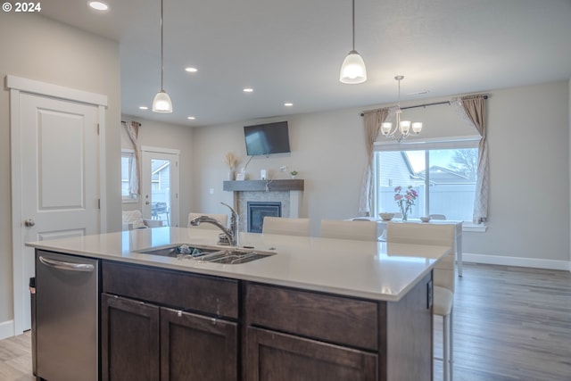 kitchen with dark brown cabinetry, dishwasher, a glass covered fireplace, light wood-type flooring, and a sink