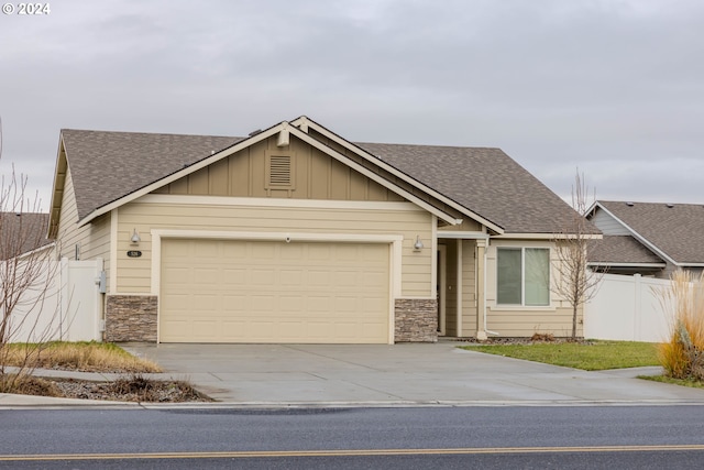 view of front of property with a garage, stone siding, concrete driveway, and fence