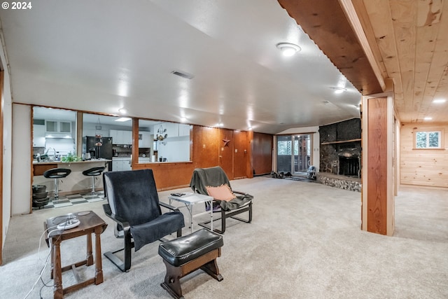 carpeted living room featuring a stone fireplace and wood walls