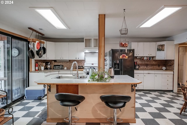 kitchen with sink, tile patterned flooring, decorative backsplash, a kitchen island with sink, and black fridge