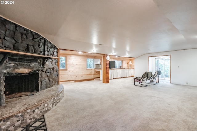 living room featuring wood walls, carpet, a stone fireplace, and vaulted ceiling