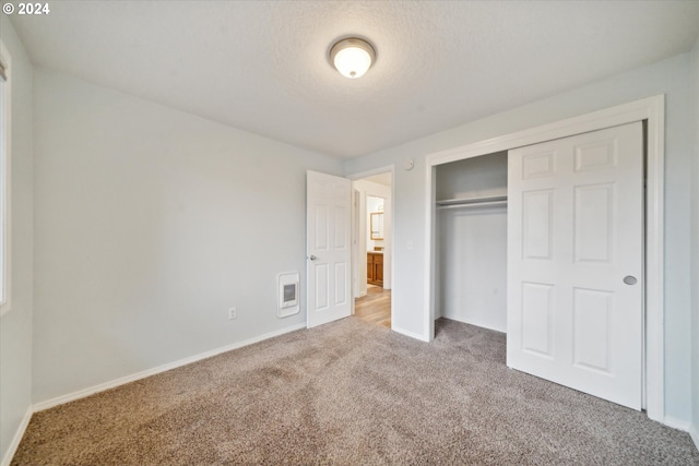 unfurnished bedroom featuring heating unit, a textured ceiling, carpet flooring, and a closet