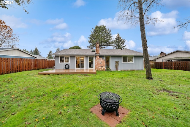 back of property with a deck, a fire pit, and a lawn