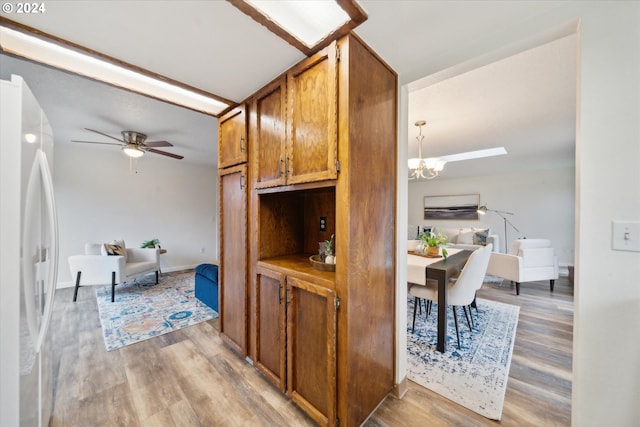 kitchen featuring hanging light fixtures, ceiling fan with notable chandelier, light hardwood / wood-style floors, and white refrigerator